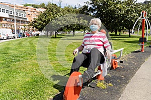 Senior woman with face mask on static bicycle machine at park