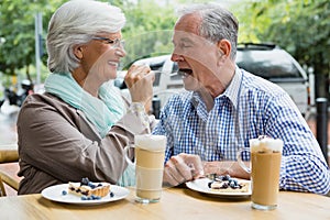 Senior woman feeding tart to man in cafÃ©