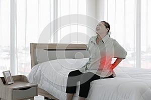 Senior woman feels back pain. sad senior older lady suffers from low-back lumbar pain sitting on bed