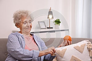 Senior woman finding orange on sofa home. Age-related memory impairment