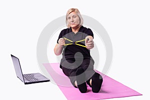 Senior woman on fitness mat training with resistance band watching online fitness program. Old person , healthy training sport at