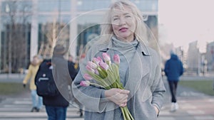 A senior woman with flowers in a big city