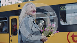 A senior woman with flowers on a tram station