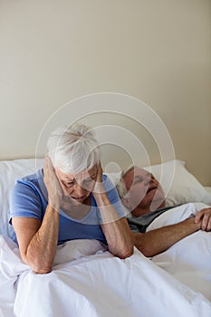 Senior woman getting disturbed with man snoring on bed