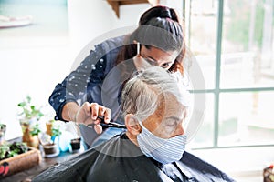 Senior woman getting a haircut at home during Covid-19 pandemic wearing face mask