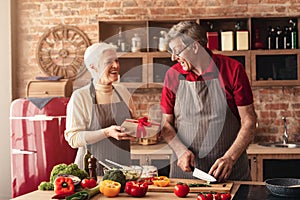 Senior woman giving gift box to husband at kitchen