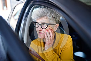 Senior woman with glasses getting out of a car.