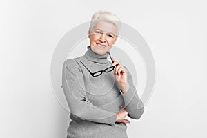 Senior woman with glasses, looking thoughtful on grey background