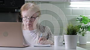 Senior woman in glasses working using laptop with serious face at home