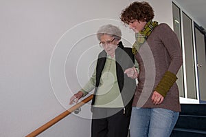 Senior woman going down stairs with helping hands of young woman