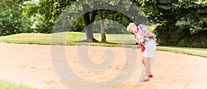 Senior woman at golf having stroke in sand bunker