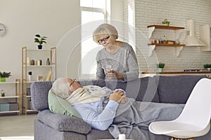 Senior woman grandmother taking care and bringing water to ill husband feeling fever