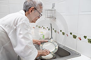 Senior woman or grandmother washing the dishes by hands in the sink,asian elderly clean dirty plates,wash dishes with dishwashing