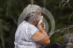 Senior woman with gray curly hair has season allergy and runny nose, sneezing.