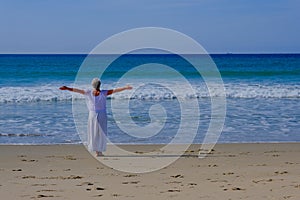 Senior woman with gray hair doing qi gong and yoga on the beach of Tarifa