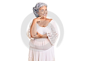 Senior woman with gray hair wearing bohemian style looking confident at the camera smiling with crossed arms and hand raised on