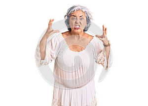 Senior woman with gray hair wearing bohemian style shouting frustrated with rage, hands trying to strangle, yelling mad