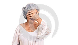 Senior woman with gray hair wearing bohemian style smiling and laughing with hand on face covering eyes for surprise