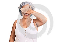 Senior woman with gray hair wearing casual clothes smiling and laughing with hand on face covering eyes for surprise