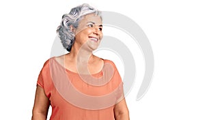 Senior woman with gray hair wearing orange tshirt looking away to side with smile on face, natural expression