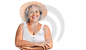 Senior woman with gray hair wearing summer hat and summer clothes happy face smiling with crossed arms looking at the camera