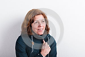 Senior woman in green jacket smiling, studio shot.