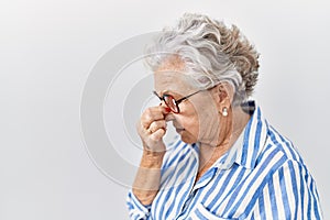 Senior woman with grey hair standing over white background tired rubbing nose and eyes feeling fatigue and headache