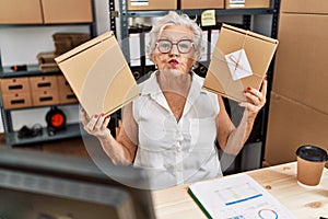 Senior woman with grey hair working at small business ecommerce looking at the camera blowing a kiss being lovely and sexy