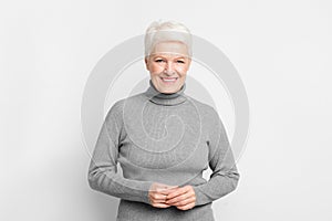 Senior woman with hands clasped, smiling on grey background