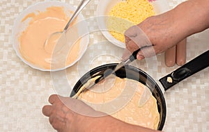Senior woman hands cut off excess dough for homemade pizza on black pan with a knife. Other ingredients are on the table