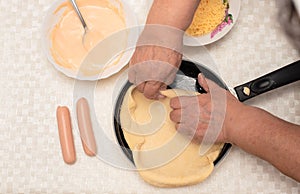 Senior woman hands knead the raw dough on black pan with oil for homemade pizza. Other ingredients are on the table. Top