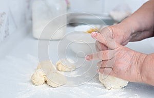 Senior woman hands kneading dough on a white kitchen table with blurred grated apple and sugar on background. Selective