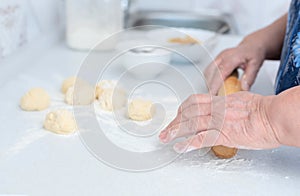 Senior woman hands rolling out the dough with a rolling pin on a white kitchen table with blurred grated apple and sugar
