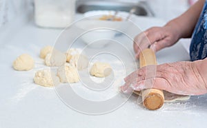 Senior woman hands rolling out the dough with a rolling pin on a white kitchen table with blurred grated apple and sugar