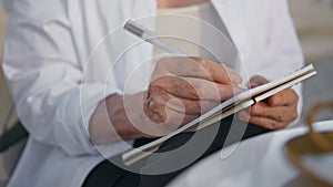 Senior woman hands writing in notebook outdoors close up. Old lady holding pen