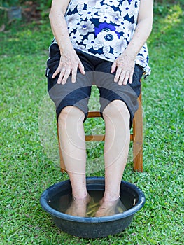A senior woman has an ankle pain treatment by spa foot with herbs in the garden. The muscles by soaking warm water that is boiled