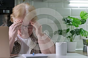 Senior woman has a headache from working on a laptop at home office