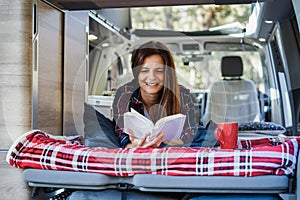 Senior woman having fun inside camper van while reading a book and drinking coffee - Focus on face