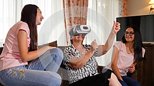 Senior woman having fun with virtual reality glasses and her granddaughters