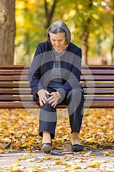 Senior woman having knee pain sitting on bench in park