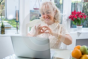 Senior woman having video call on laptop and showing heart shape