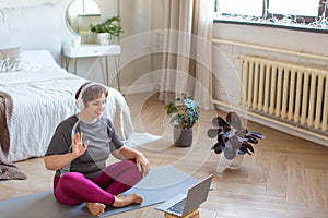 Senior woman in headphones having video conversation with a trainer online before a Pilates workout.