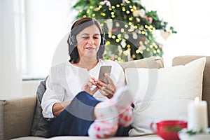 A senior woman with headphones listening to music at home at Christmas time.