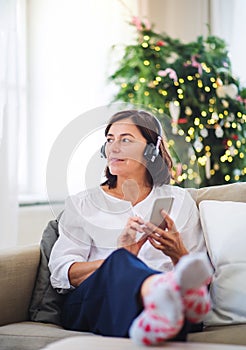 A senior woman with headphones listening to music at home at Christmas time.