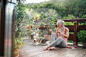 A senior woman with headphones outdoors on a terrace, resting after exercise.