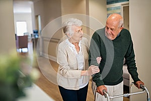 Senior woman helping disabled husband walk at medical clinic