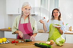 Senior woman and her adult daughter cooking salad together