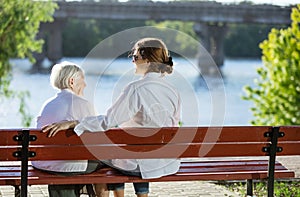 Senior woman and her adult granddaughter sitting on bench in par