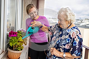 Senior woman and her adult granddaughter watering plants on the balcony