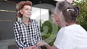 Senior woman and her daughter having fun, holding hands sitting on bench in city. Two generation women holding hands